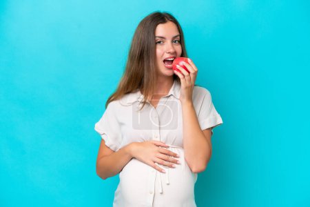 Photo for Young caucasian woman isolated on blue background pregnant and holding an apple - Royalty Free Image
