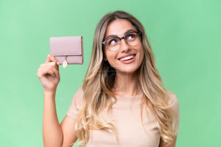Photo for Young Uruguayan woman holding a wallet over isolated background looking up while smiling - Royalty Free Image