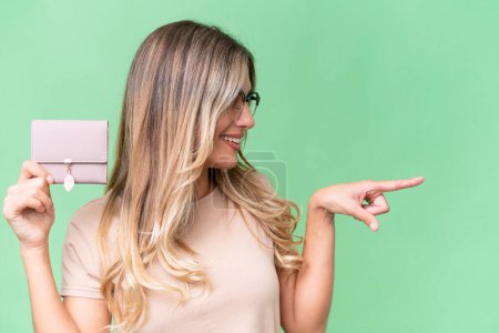 Photo for Young Uruguayan woman holding a wallet over isolated background pointing to the side to present a product - Royalty Free Image