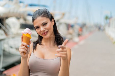 Foto de Joven mujer bonita con un helado de corneta al aire libre apunta con el dedo a usted con una expresión de confianza - Imagen libre de derechos