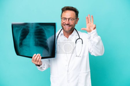 Foto de Médico traumatólogo profesional de mediana edad aislado sobre fondo azul feliz y contando cuatro con los dedos - Imagen libre de derechos