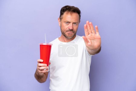 Foto de Hombre caucásico de mediana edad sosteniendo soda aislada sobre fondo púrpura haciendo gesto de parada - Imagen libre de derechos