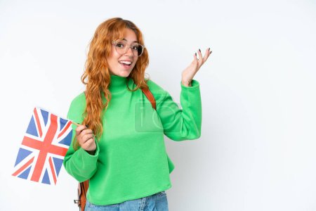 Téléchargez les photos : Jeune femme caucasienne tenant un drapeau du Royaume-Uni isolé sur fond blanc étendant les mains sur le côté pour inviter à venir - en image libre de droit