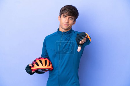 Téléchargez les photos : Young cyclist caucasian man isolated on purple background showing thumb down with negative expression - en image libre de droit