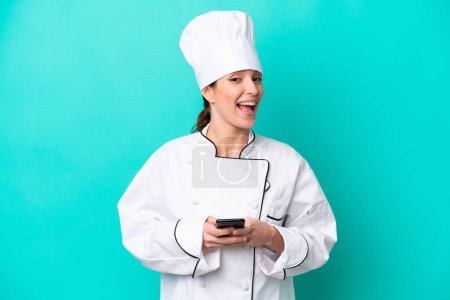 Photo for Young caucasian chef woman isolated on blue background surprised and sending a message - Royalty Free Image