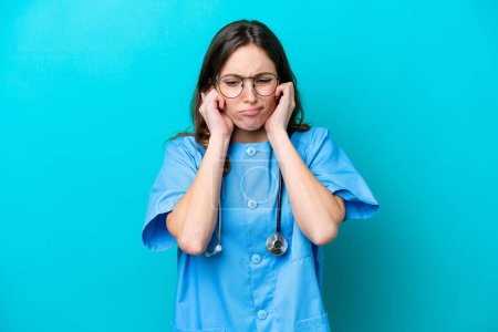 Foto de Joven cirujana doctora aislada sobre fondo azul frustrada y cubriendo oídos - Imagen libre de derechos