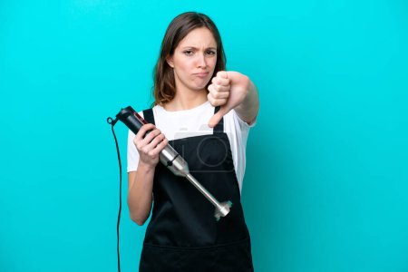 Photo for Young caucasian cooker woman using hand blender isolated on blue background showing thumb down with negative expression - Royalty Free Image