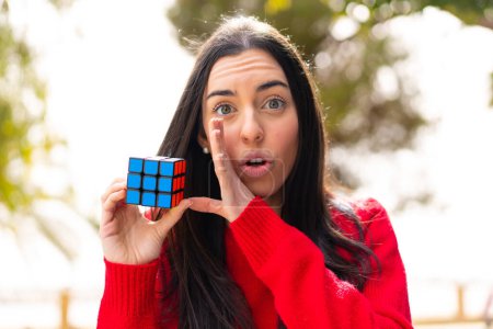 Photo for Young woman holding a three dimensional puzzle cube at outdoors whispering something - Royalty Free Image