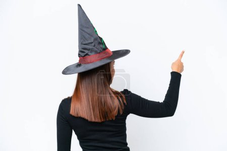 Téléchargez les photos : Jeune costume de femme caucasienne comme sorcière isolée sur fond blanc pointant vers l'arrière avec l'index - en image libre de droit