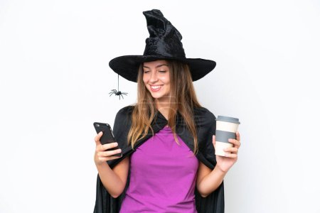 Téléchargez les photos : Jeune costume de femme caucasienne comme sorcière isolée sur fond blanc tenant du café à emporter et un mobile - en image libre de droit