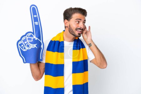 Téléchargez les photos : Jeune fan de sport homme isolé sur fond blanc écoutant quelque chose en mettant la main sur l'oreille - en image libre de droit
