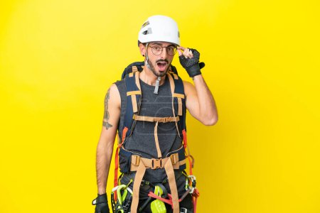 Téléchargez les photos : Jeune alpiniste caucasien isolé sur fond jaune avec des lunettes et surpris - en image libre de droit