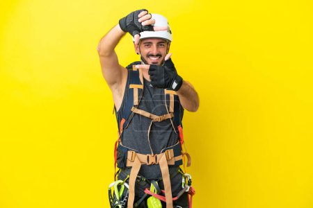 Foto de Joven escalador caucásico aislado sobre fondo amarillo enfocando la cara. Símbolo de encuadre - Imagen libre de derechos