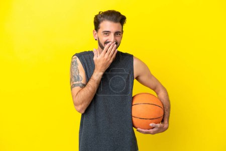 Foto de Guapo joven jugador de baloncesto hombre aislado sobre fondo amarillo feliz y sonriente boca cubierta con la mano - Imagen libre de derechos