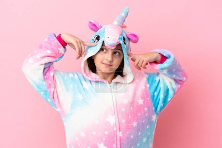 Foto de Pequeña mujer caucásica vistiendo un pijama unicornio aislado sobre fondo rosa teniendo dudas y pensando - Imagen libre de derechos