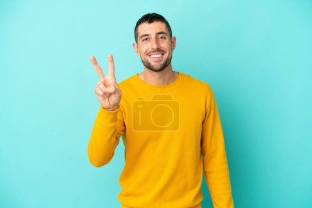 Photo for Young handsome caucasian man isolated on blue background smiling and showing victory sign - Royalty Free Image