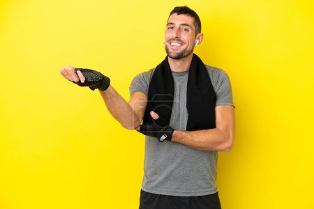 Foto de Joven hombre caucásico deporte aislado sobre fondo amarillo extendiendo las manos a un lado para invitar a venir - Imagen libre de derechos