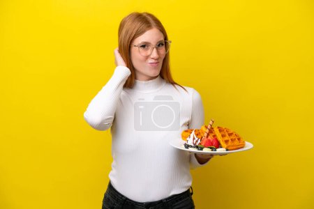 Photo for Young redhead woman holding waffles isolated on yellow background having doubts - Royalty Free Image