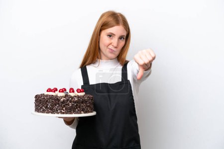 Photo for Young redhead woman holding birthday cake isolated on white background showing thumb down with negative expression - Royalty Free Image
