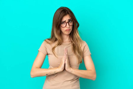 Photo for Young caucasian woman isolated on blue background keeps palm together. Person asks for something - Royalty Free Image