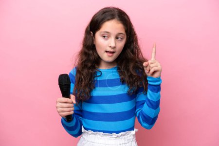Téléchargez les photos : Petite chanteuse ramassant un microphone isolé sur fond rose dans l'intention de réaliser la solution tout en levant le doigt - en image libre de droit