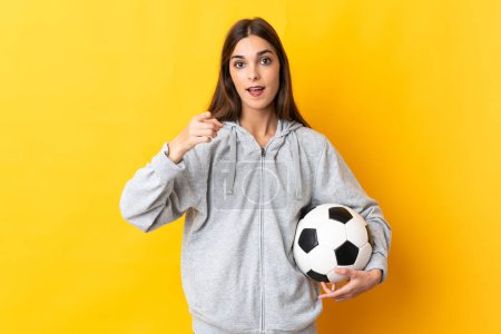 Photo for Young football player woman isolated on yellow background surprised and pointing front - Royalty Free Image