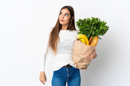 Téléchargez les photos : Jeune femme caucasienne acheter de la nourriture isolée sur fond blanc penser une idée tout en levant les yeux - en image libre de droit