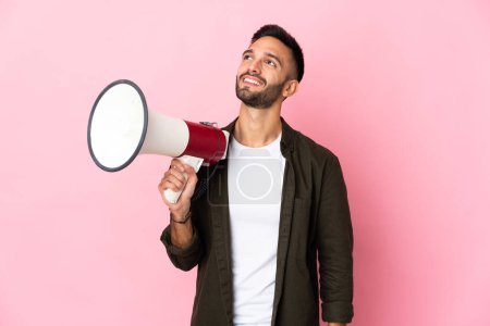 Téléchargez les photos : Young caucasian man isolated on pink background holding a megaphone and looking up while smiling - en image libre de droit