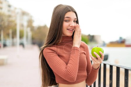 Téléchargez les photos : Adolescente avec une pomme à l'extérieur chuchotant quelque chose - en image libre de droit