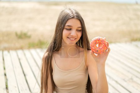 Photo for Teenager girl holding a donut at outdoors with happy expression - Royalty Free Image