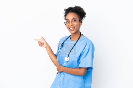 Foto de Joven cirujana afroamericana doctora aislada sobre fondo blanco apuntando con el dedo hacia un lado - Imagen libre de derechos
