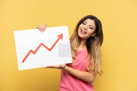 Photo for Young Russian girl isolated on yellow background holding a sign with a growing statistics arrow symbol - Royalty Free Image