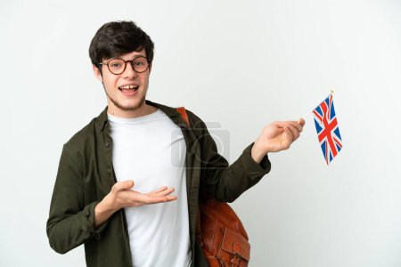 Téléchargez les photos : Jeune homme russe tenant un drapeau du Royaume-Uni isolé sur fond blanc étendant les mains sur le côté pour inviter à venir - en image libre de droit