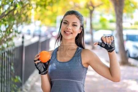 Téléchargez les photos : Jeune jolie femme sportive tenant une orange à l'extérieur fière et satisfaite de soi - en image libre de droit
