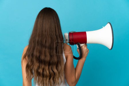 Photo for Young hispanic woman over isolated blue background holding a megaphone and in back position - Royalty Free Image