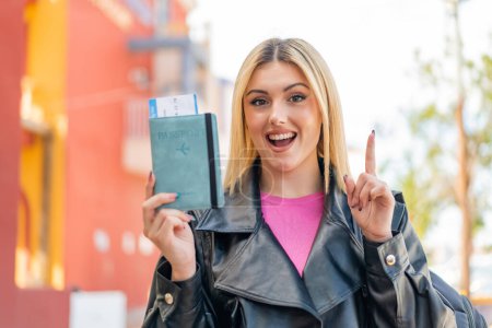 Foto de Joven mujer rubia bonita sosteniendo un pasaporte al aire libre señalando una gran idea - Imagen libre de derechos