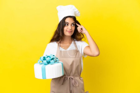 Téléchargez les photos : Jeune chef pâtissier caucasien femme avec un gros gâteau isolé sur fond jaune ayant des doutes et la pensée - en image libre de droit