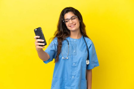 Téléchargez les photos : Jeune chirurgien médecin femme isolée sur fond jaune faire un selfie - en image libre de droit