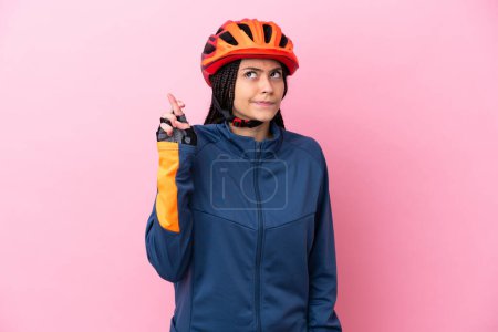 Téléchargez les photos : Adolescente cycliste fille isolée sur fond rose avec les doigts croisés et souhaitant le meilleur - en image libre de droit