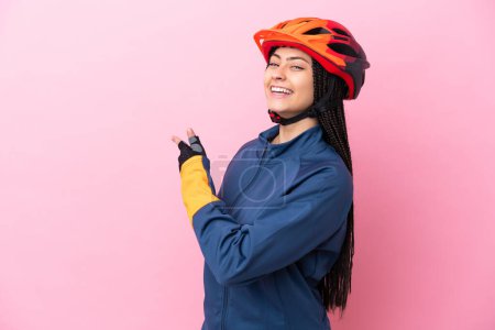 Téléchargez les photos : Adolescente cycliste fille isolé sur fond rose pointant vers l'arrière - en image libre de droit