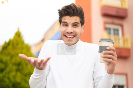 Téléchargez les photos : Jeune homme caucasien tenant un café à emporter à l'extérieur avec expression faciale choquée - en image libre de droit