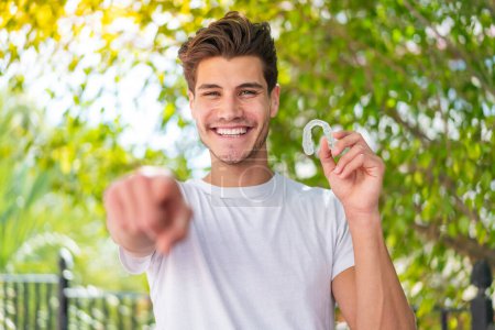 Téléchargez les photos : Jeune homme caucasien tenant des bretelles invisibles à l'extérieur pointe doigt à vous avec une expression confiante - en image libre de droit