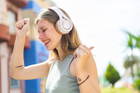 Téléchargez les photos : Jeune femme blonde à l'extérieur écouter de la musique et danser - en image libre de droit