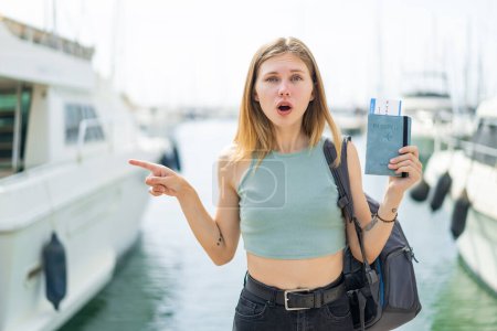 Photo for Young blonde woman holding a passport at outdoors surprised and pointing side - Royalty Free Image