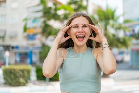 Foto de Mujer rubia joven con gafas al aire libre con expresión sorpresa - Imagen libre de derechos