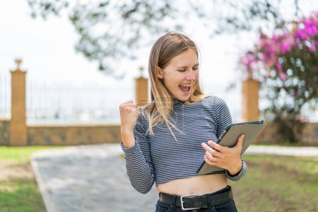 Téléchargez les photos : Jeune femme blonde tenant une tablette en plein air célébrant une victoire - en image libre de droit