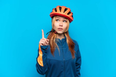 Photo for Young cyclist girl isolated on blue background thinking an idea pointing the finger up - Royalty Free Image