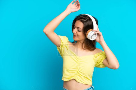 Foto de Joven mujer caucásica aislada sobre fondo azul escuchando música y bailando - Imagen libre de derechos