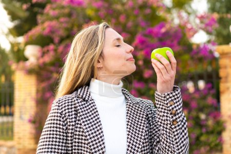Foto de Mujer rubia joven con una manzana al aire libre - Imagen libre de derechos