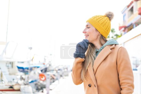 Téléchargez les photos : Jeune femme blonde portant une veste d'hiver à l'extérieur pensant une idée et regardant côté - en image libre de droit